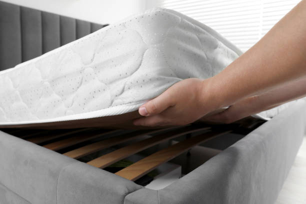 Woman putting soft light green mattress on gray bed indoors, closeup